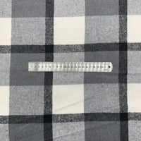 Une règle en plastique transparent de 20 cm est posée horizontalement sur la flanelle à carreaux en polyester-coton de Longon Craft France, en noir, blanc et gris, parfaite pour les robes d'automne, les chemises et les projets de couture.
