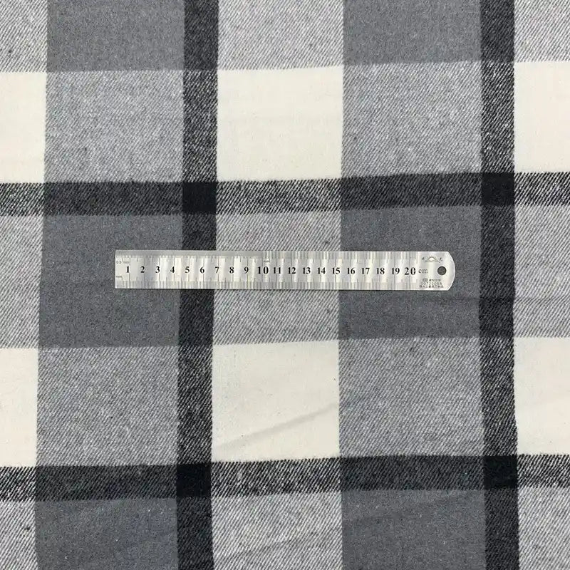 Une règle en plastique transparent de 20 cm est posée horizontalement sur la flanelle à carreaux en polyester-coton de Longon Craft France, en noir, blanc et gris, parfaite pour les robes d'automne, les chemises et les projets de couture.