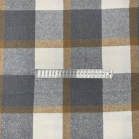 Une règle en plastique transparente de 20 cm repose sur le "Tissu en flanelle à carreaux pour l'automne au mètre" de Longon Craft France, un tissu écossais doux en polyester et coton, parfaitement aligné avec ses carreaux gris, bruns et blancs.