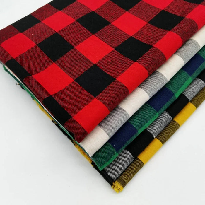 Cinq pièces empilées du douillet tissu flanelle à carreaux au mètre de Longon Craft France, aux motifs rouge/noir, noir/blanc, bleu/noir, vert/noir et jaune/noir, sont présentées sur une surface blanche.