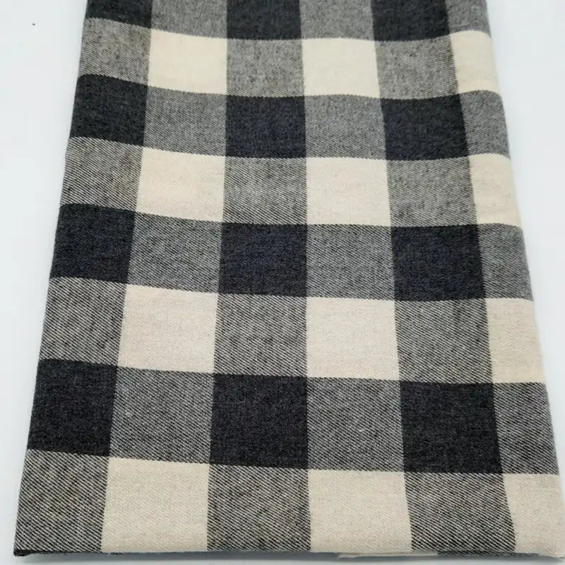 Un morceau de Tissu flanelle à carreaux au mètre de Longon Craft France, présentant un motif à carreaux noir, blanc et gris, est posé à plat sur une surface blanche - une flanelle polyester-coton parfaite pour les projets de couture festifs.
