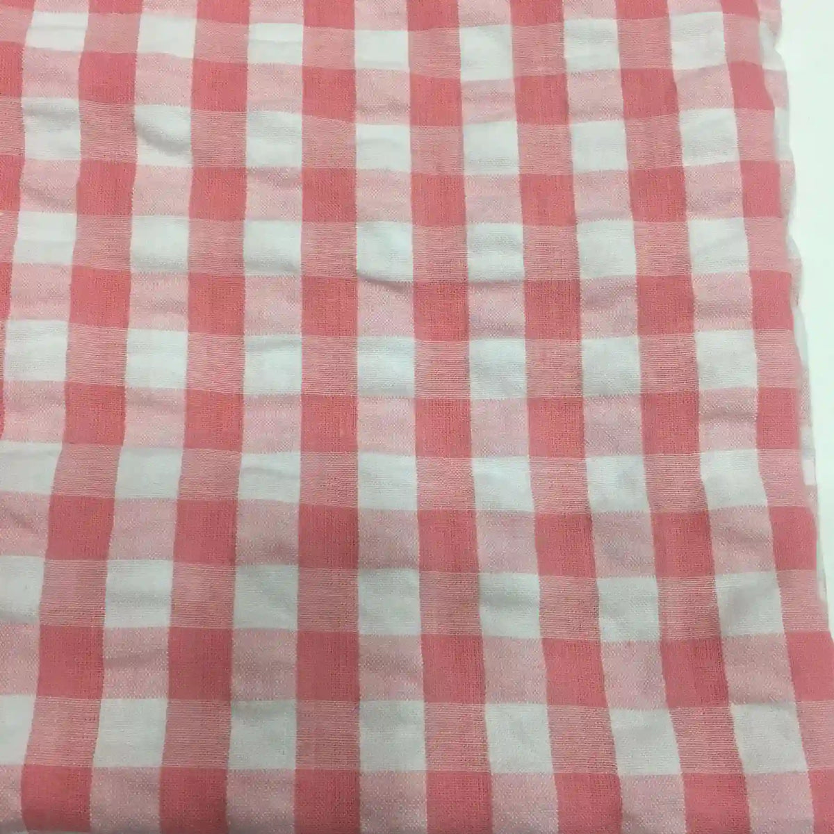 Découvrez le Tissu seersucker à carreaux au mètre de Longan Craft France : un seersucker vichy rose et blanc, léger et légèrement froissé, idéal pour vêtements d'été. Présenté à plat avec des carreaux réguliers.