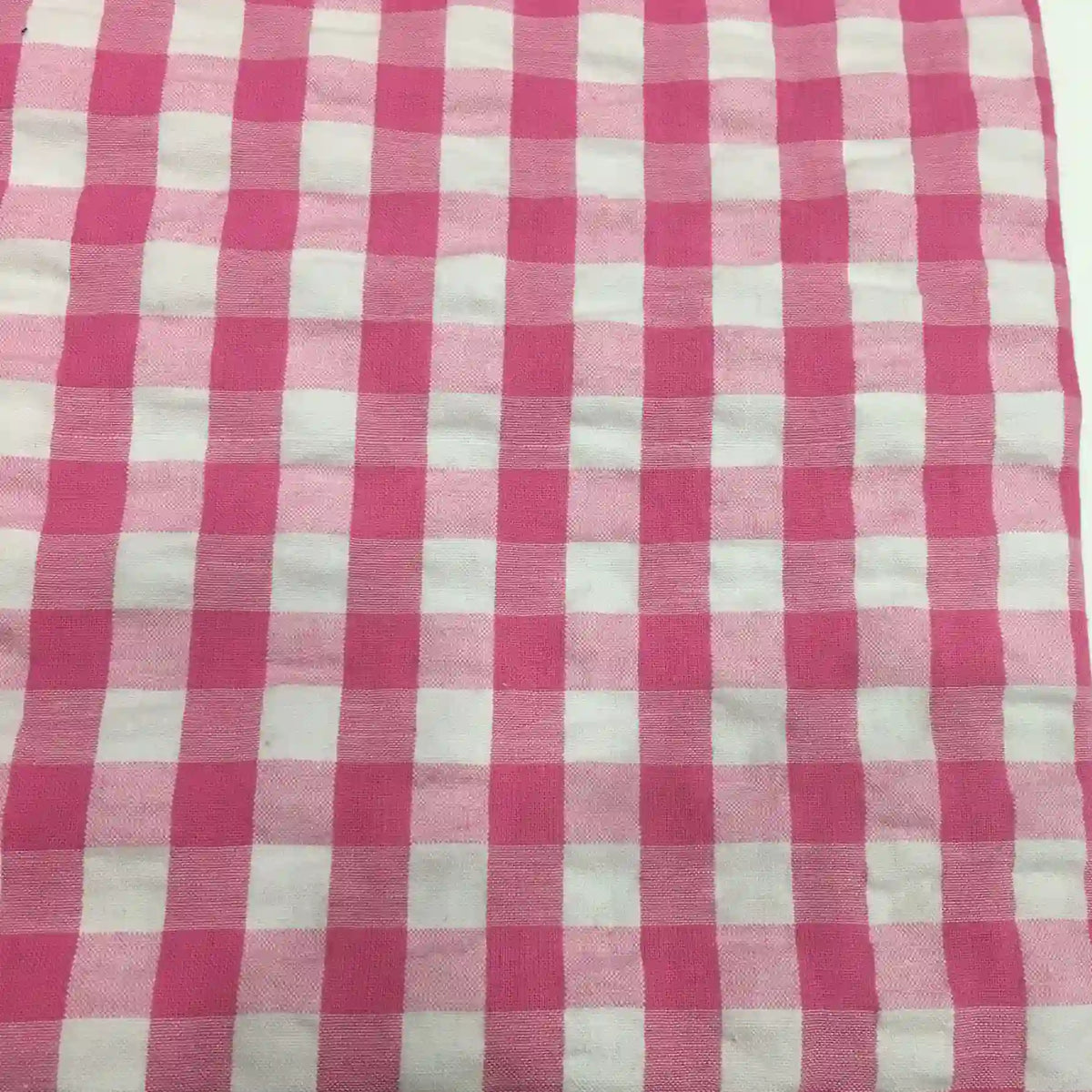 Un gros plan du tissu seersucker à carreaux au mètre de Longan Craft France montre un motif vichy rose et blanc avec des carrés régulièrement espacés et une finition légèrement texturée, idéale pour les vêtements d'été légers.