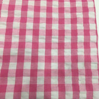 Un gros plan du tissu seersucker à carreaux au mètre de Longan Craft France montre un motif vichy rose et blanc avec des carrés régulièrement espacés et une finition légèrement texturée, idéale pour les vêtements d'été légers.