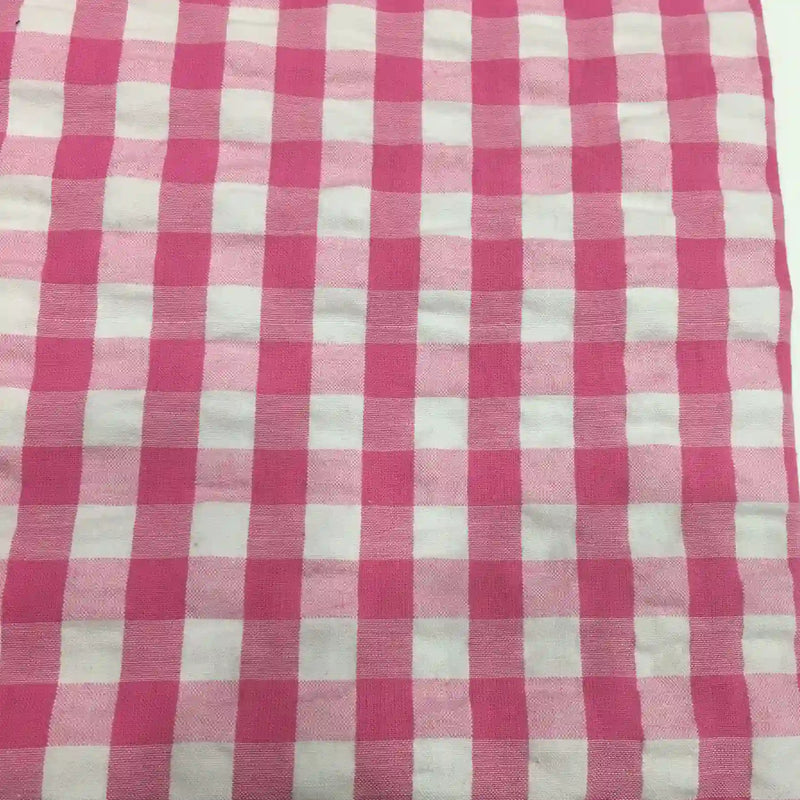 Un gros plan du tissu seersucker à carreaux au mètre de Longan Craft France montre un motif vichy rose et blanc avec des carrés régulièrement espacés et une finition légèrement texturée, idéale pour les vêtements d'été légers.