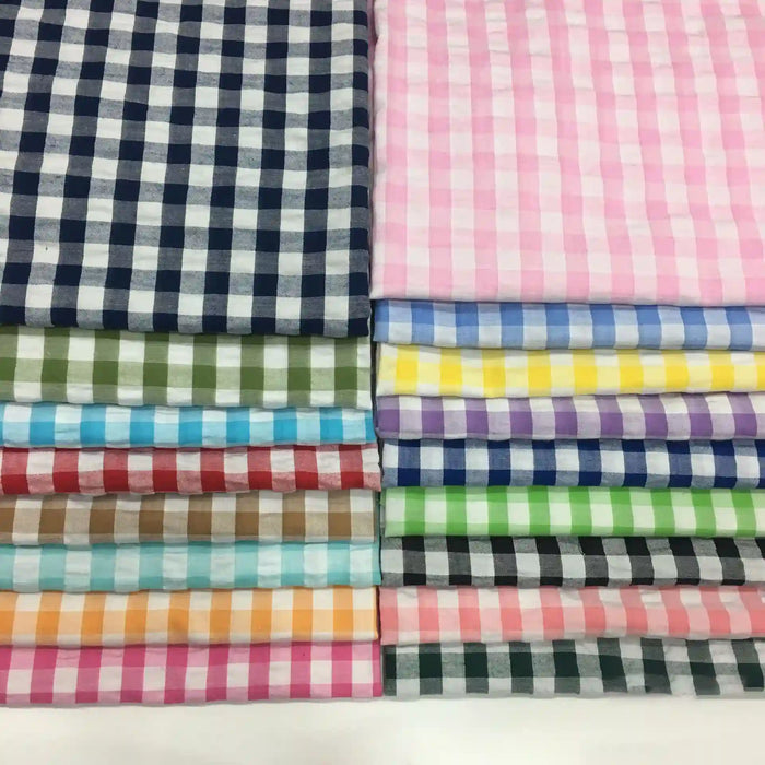 Des tissus seersucker à motif vichy de Longan Craft France, soigneusement empilés : colonnes à gauche en tons foncés, à droite en couleurs claires et pastel-idéals pour des vêtements d'été légers.