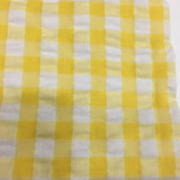 Un gros plan du Tissu seersucker à carreaux au mètre de Longan Craft France montre un motif vichy jaune et blanc dans un seersucker léger, idéal pour les vêtements d'été et fabriqué à partir d'un mélange de coton ou de polyester.
