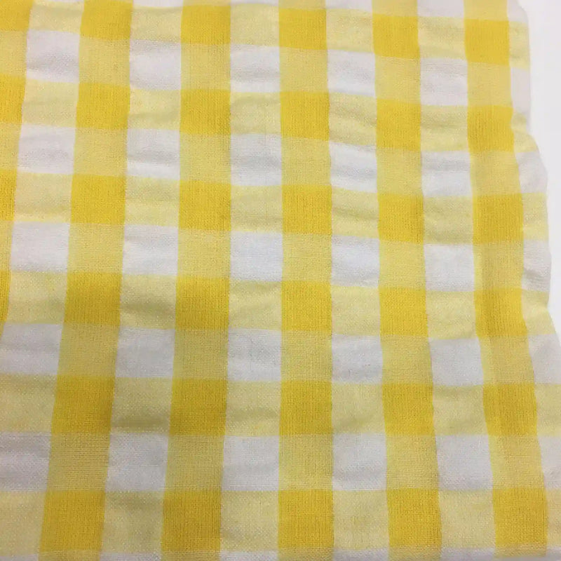 Un gros plan du Tissu seersucker à carreaux au mètre de Longan Craft France montre un motif vichy jaune et blanc dans un seersucker léger, idéal pour les vêtements d'été et fabriqué à partir d'un mélange de coton ou de polyester.