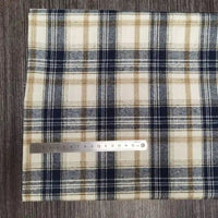 Un morceau de tissu flanelle à carreaux polyester-coton de Longon Craft France, à carreaux beige, marine et blanc, est posé sur du bois avec une règle métallique de 15 cm pour l'échelle. Idéal pour les vêtements d'automne des bébés et vendu au mètre.