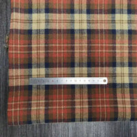 Un tissu rayé rouge, beige et bleu foncé, le tissu flanelle à carreaux polyester-coton de Longon Craft France, est posé sur du bois, avec une règle en métal (0-16 cm) placée sur ce tissu d'automne confortable pour la couture de vêtements de bébé.