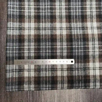 Une règle métallique avec des marques en centimètres et en millimètres est placée à côté du tissu flanelle à carreaux polyester-coton au mètre de Longon Craft France, idéal pour l'automne et la couture de vêtements bébé, présenté sur une surface en bois.