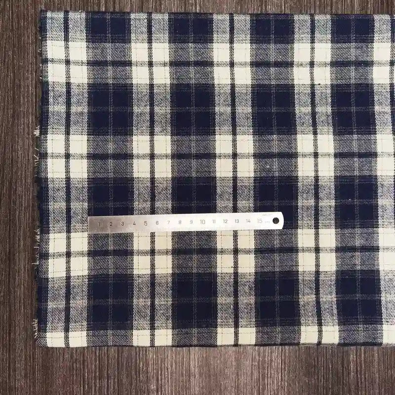 A piece of Longon Craft France Tissu flanelle à carreaux polyester-coton, idéal pour l'automne et la couture de vêtements bébé, is posé à plat sur du bois avec une règle métallique de 20 cm placée horizontalement dessus.