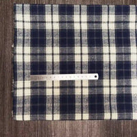 A piece of Longon Craft France Tissu flanelle à carreaux polyester-coton, idéal pour l'automne et la couture de vêtements bébé, is posé à plat sur du bois avec une règle métallique de 20 cm placée horizontalement dessus.