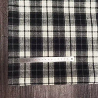 Un morceau de tissu flanelle à carreaux polyester-coton au mètre de Longon Craft France est présenté sur du bois, avec à côté une règle en métal indiquant une échelle de 0 à 15 cm. Cette flanelle confortable est idéale pour l'automne et la couture de vêtements pour bébés.