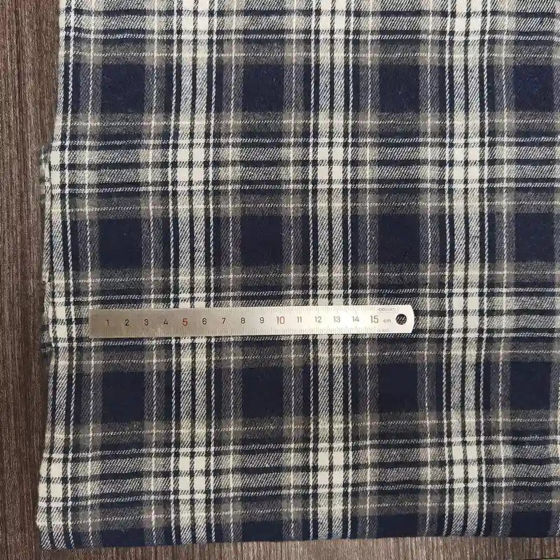 Un morceau de Tissu flanelle à carreaux polyester-coton au mètre de Longon Craft France est posé sur une surface en bois, avec une règle métallique de 20 cm placée en travers pour montrer l'échelle. Idéal pour les projets de couture d'automne et de vêtements pour bébés.