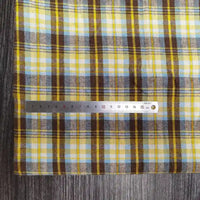 Une règle métallique Longon Craft France mesure un tissu flanelle à carreaux polyester-coton (bébé, automne) à carreaux jaunes, bruns et bleus sur une surface grise. L'échelle des centimètres va de 0 à 15.