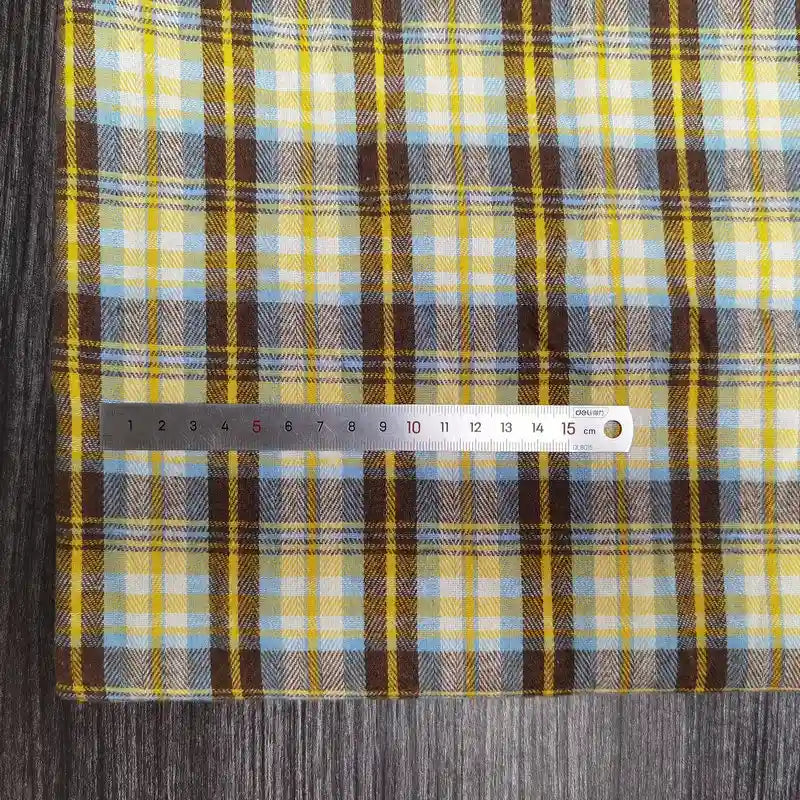 Une règle métallique Longon Craft France mesure un tissu flanelle à carreaux polyester-coton (bébé, automne) à carreaux jaunes, bruns et bleus sur une surface grise. L'échelle des centimètres va de 0 à 15.