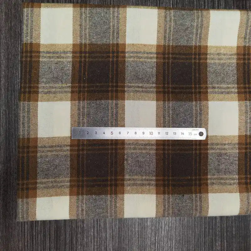 Une règle en argent de 18 cm est posée sur un tissu Longon Craft France Tissu flanelle à carreaux polyester-coton, un tissu flanelle d'automne confortable pour les vêtements de bébé, présenté sur une surface texturée foncée.