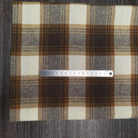 Une règle en argent de 18 cm est posée sur un tissu Longon Craft France Tissu flanelle à carreaux polyester-coton, un tissu flanelle d'automne confortable pour les vêtements de bébé, présenté sur une surface texturée foncée.