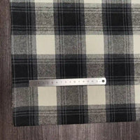 A tissu flanelle à carreaux polyester-coton Longon Craft France, en noir, blanc et gris, est posé sur du bois. Un mètre ruban montre 16 cm-idéal pour la couture de vêtements bébé ou l'automne.