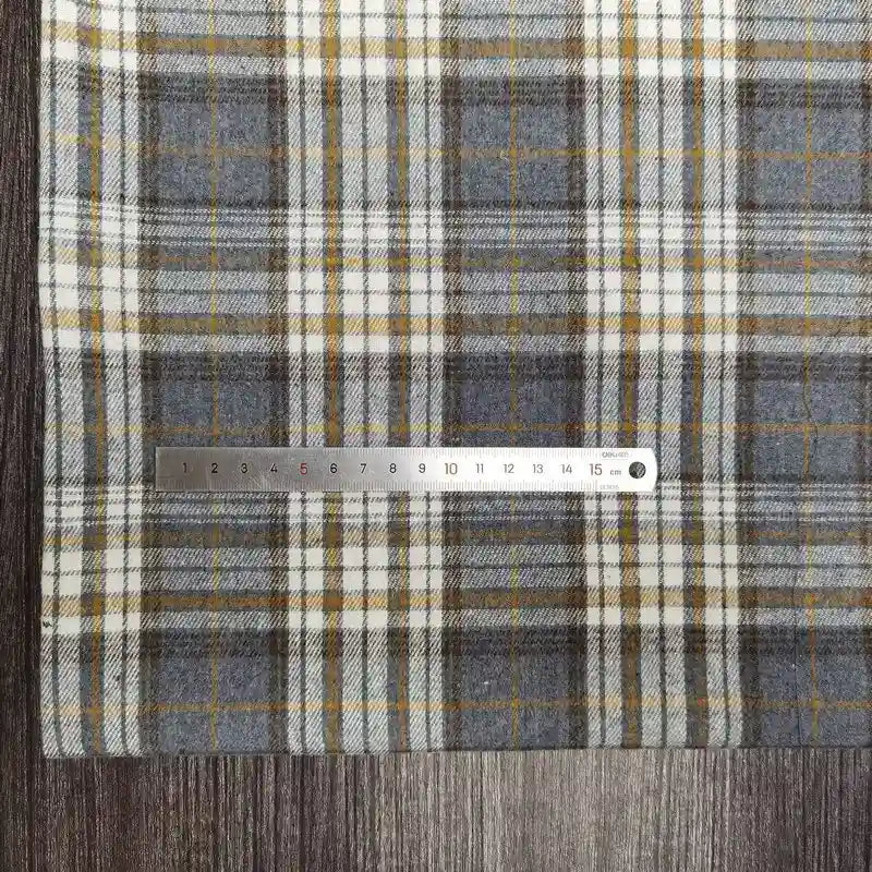 Une règle métallique Longon Craft France repose sur un tissu polyester-coton flanelle à carreaux, idéal pour la couture d'automne ou de vêtements de bébé, mesurant de 1 à 15 cm sur une surface en bois.