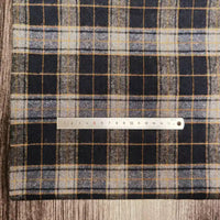 Une règle en métal est posée sur le tissu flanelle à carreaux polyester-coton au mètre de Longon Craft France, un tissu d'automne douillet parfait pour coudre des vêtements de bébé, avec une surface en bois en dessous. La règle mesure environ 16 centimètres.