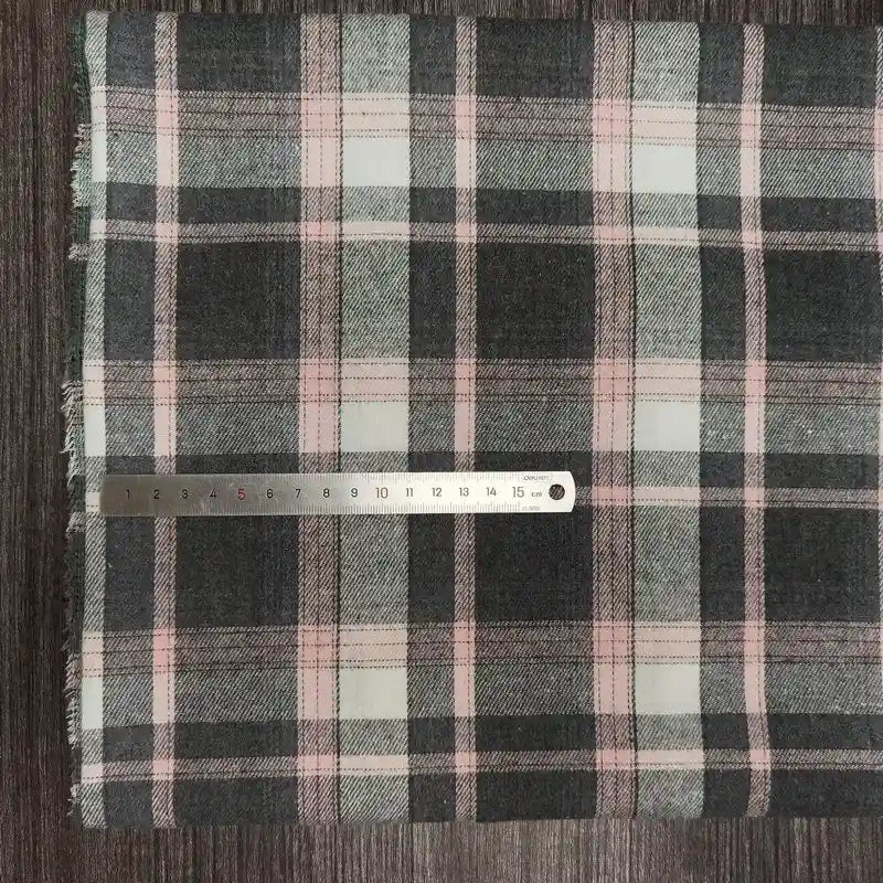 Une règle en métal de 20 cm repose sur le tissu flanelle à carreaux polyester-coton de Longon Craft France, qui présente des rayures noires, blanches et roses - parfaites pour les vêtements d'automne ou la couture des bébés - sur une surface texturée.