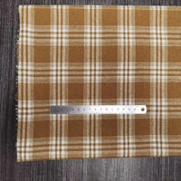 Un morceau de Tissu flanelle à carreaux polyester-coton au mètre de Longon Craft France, idéal pour vêtements bébé ou automne, est posé sur une surface en bois sombre avec une règle métallique de 15 cm placée horizontalement dessus.