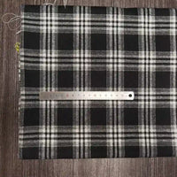 Un morceau de Tissu flanelle à carreaux polyester-coton Longon Craft France est posé à plat sur une surface sombre avec une règle métallique en travers, mesurant environ 15 cm. Ce tissu flanelle confortable est idéal pour les projets de couture de vêtements d'automne pour bébés.