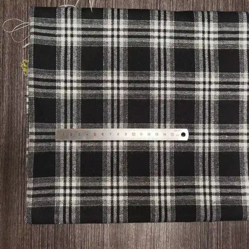 Un morceau de Tissu flanelle à carreaux polyester-coton Longon Craft France est posé à plat sur une surface sombre avec une règle métallique en travers, mesurant environ 15 cm. Ce tissu flanelle confortable est idéal pour les projets de couture de vêtements d'automne pour bébés.