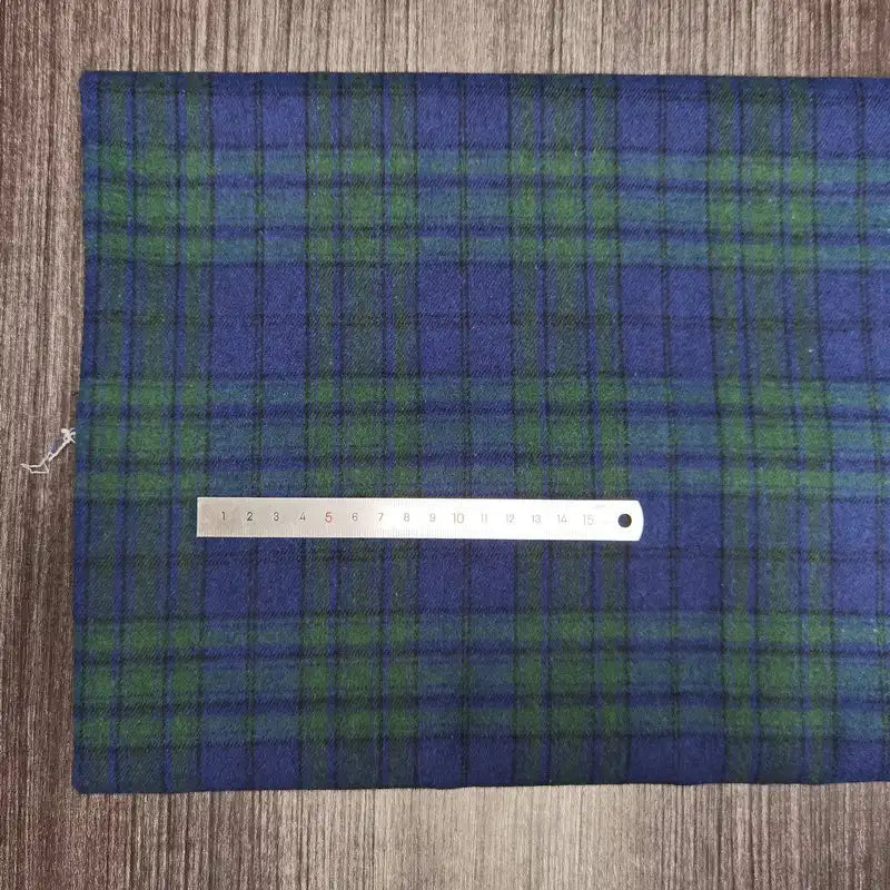 Une règle métallique de 15 cm repose sur le tissu écossais en flanelle de polyester-coton de Longon Craft France, un textile d'automne confortable idéal pour les vêtements de bébé, présenté sur une surface en bois.
