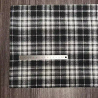 Une règle métallique de 30 cm repose sur le tissu flanelle à carreaux polyester-coton de Longon Craft France, un tissu flanelle confortable pour les vêtements d'automne et de bébé, posé à plat sur une surface en bois sombre.