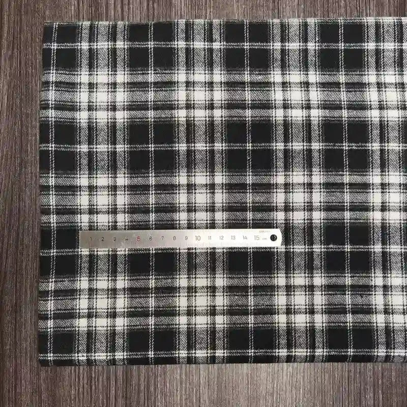 Une règle métallique de 30 cm repose sur le tissu flanelle à carreaux polyester-coton de Longon Craft France, un tissu flanelle confortable pour les vêtements d'automne et de bébé, posé à plat sur une surface en bois sombre.
