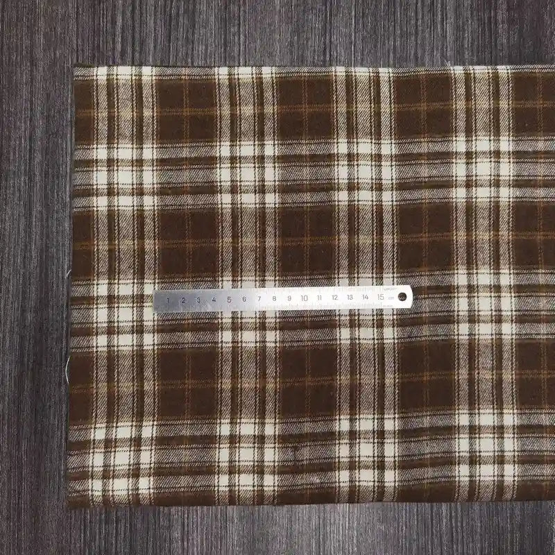 Un morceau de Longon Craft France Tissu flanelle à carreaux polyester-coton est disposé sur une surface sombre avec une règle métallique en centimètres, idéal pour les projets de couture de vêtements d'automne pour bébés.