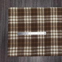 Un morceau de Longon Craft France Tissu flanelle à carreaux polyester-coton est disposé sur une surface sombre avec une règle métallique en centimètres, idéal pour les projets de couture de vêtements d'automne pour bébés.