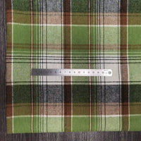 Une règle argentée trône sur le Tissu flanelle à carreaux polyester-coton au mètre de Longon Craft France, idéal pour les vêtements d'hiver. Ce tissu d'automne doux pour les vêtements de bébé repose sur une surface grise texturée, mesurant environ 15 cm.