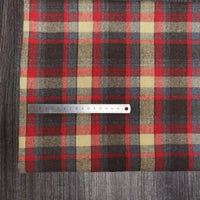 Une règle métallique de 15 cm repose sur le tissu flanelle à carreaux polyester-coton au mètre de Longon Craft France, un tissu d'automne confortable pour les vêtements de bébé, présenté sur une surface en bois.