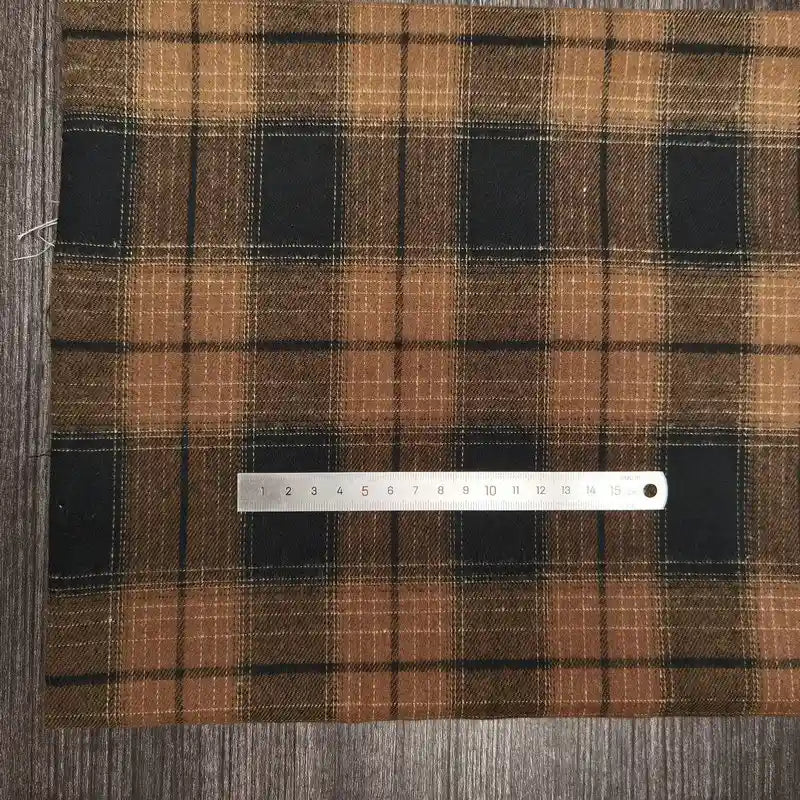 Une règle métallique en centimètres est posée sur un tissu Longon Craft France tissu flanelle à carreaux polyester-coton, idéal pour la couture d'automne et de vêtements de bébé, présenté sur une surface en bois.