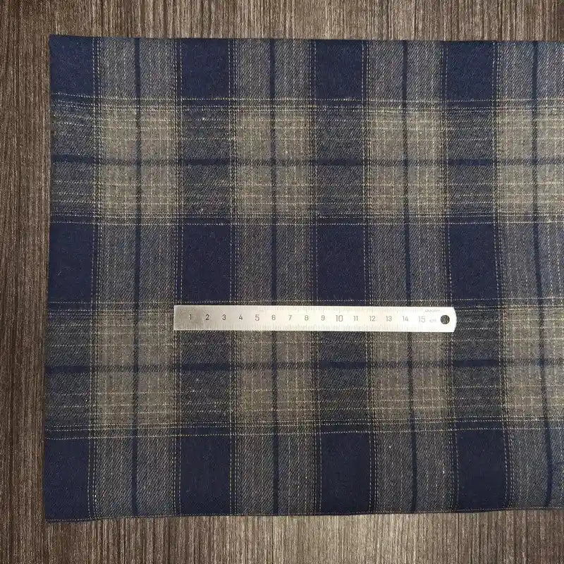 Une règle métallique avec des repères en centimètres repose sur le Tissu flanelle à carreaux en polyester-coton de Longon Craft France, un tissu flanelle d'automne confortable pour les vêtements de bébé, présenté sur une surface en bois.