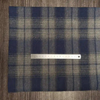 Une règle métallique avec des repères en centimètres repose sur le Tissu flanelle à carreaux en polyester-coton de Longon Craft France, un tissu flanelle d'automne confortable pour les vêtements de bébé, présenté sur une surface en bois.