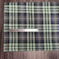 A coupon de tissu flanelle à carreaux polyester-coton Longon Craft France est posé sur une surface en bois avec une règle métallique posée dessus, idéal pour la couture de vêtements bébé ou d'automne.