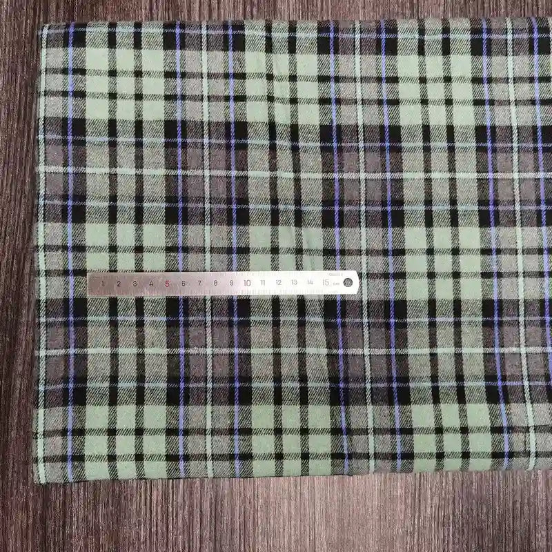 A coupon de tissu flanelle à carreaux polyester-coton Longon Craft France est posé sur une surface en bois avec une règle métallique posée dessus, idéal pour la couture de vêtements bébé ou d'automne.