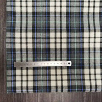 Une règle en métal (18 cm) est posée horizontalement sur le tissu flanelle à carreaux polyester-coton de Longon Craft France, un tissu douillet pour les vêtements d'automne et de bébé, dont les lignes noires, blanches, bleues et vertes sont disposées sur une surface en bois sombre.