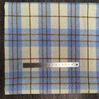 Une pièce de Longon Craft France Tissu flanelle à carreaux polyester-coton au mètre, en bleu clair, beige et marron, est posé à plat avec une règle pour l'échelle. Idéal pour vêtements d'automne ou couture de vêtements bébé.