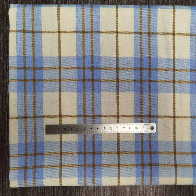Une pièce de Longon Craft France Tissu flanelle à carreaux polyester-coton au mètre, en bleu clair, beige et marron, est posé à plat avec une règle pour l'échelle. Idéal pour vêtements d'automne ou couture de vêtements bébé.