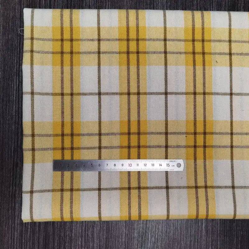 Un morceau plié de la flanelle à carreaux en polyester-coton de Longon Craft France, destinée aux vêtements d'automne pour bébés, est posé sur une surface sombre, avec une règle métallique de 15 cm placée le long de son bord.