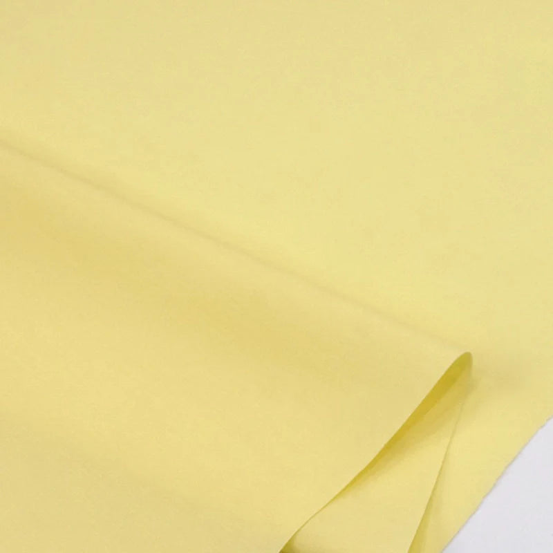 Un gros plan de Popeline polyester-coton au mètre de Longan Craft France montre un tissu popeline uni à armure toile lisse et jaune clair, non texturé et aux couleurs uniformes - idéal pour les peignoirs, les chemises et les couches.
