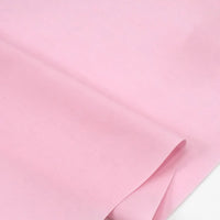 Gros plan sur le Popeline polyester-coton au mètre de Longan Craft France, un tissu popeline à armure toile, doux et respirant, de couleur rose pâle, partiellement plié sur un fond blanc. Convient pour les robes, les chemises et les nappes.