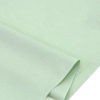 Le "Popeline polyester-coton au mètre" de Longan Craft France en vert clair s'étend à plat avec un coin plié, mettant en valeur son tissage popeline lisse, doux et respirant, idéal pour les peignoirs, les chemises et les nappes.