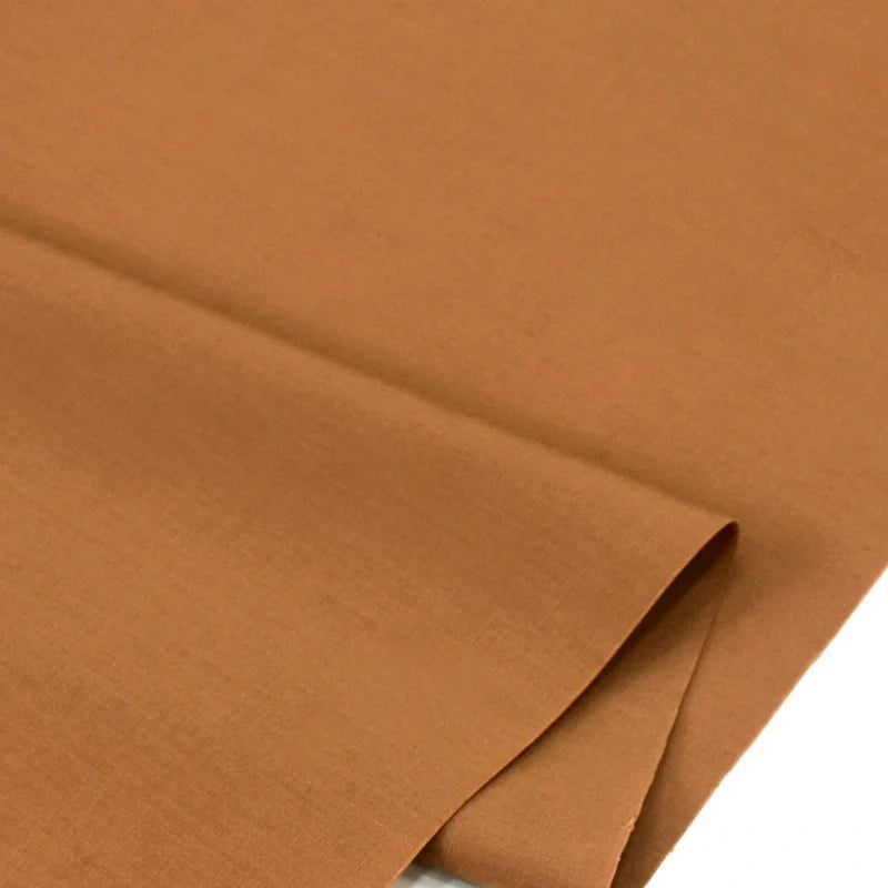 Gros plan sur Popeline polyester-coton au mètre de Longan Craft France, un tissu popeline uni à armure toile, marron clair, doux et respirant, soigneusement plié pour montrer sa texture lisse et régulière pour les peignoirs, chemises et langes.
